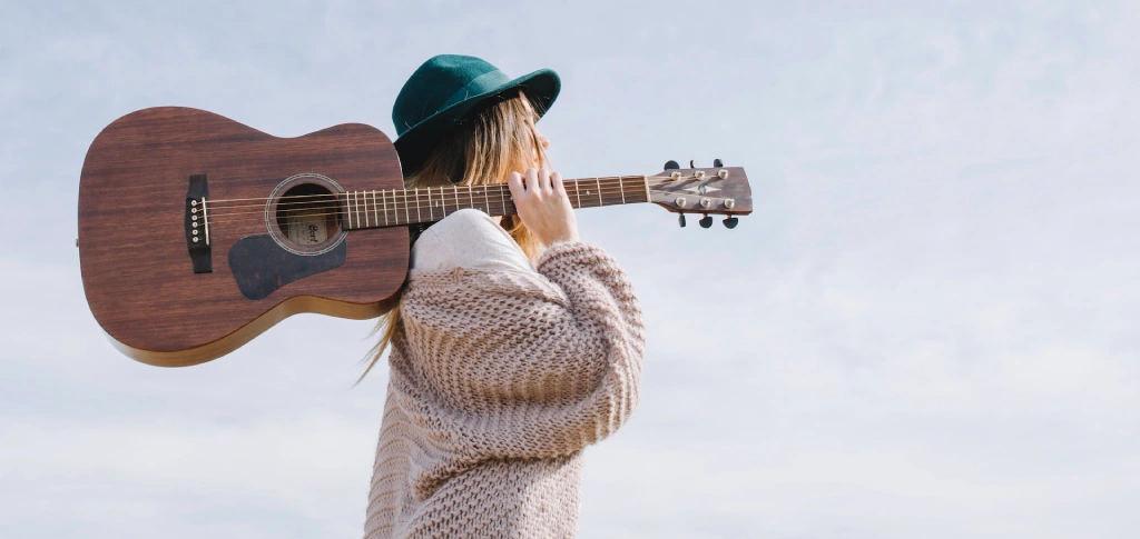 Photo d'une jeune femme avec un chapeau et une guitare sur l'épaule. 